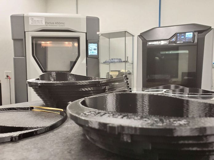 Don Schmuacher Motorsports' two Stratasys FDM 3D printers (background) are operating around-the-clock to produce headbands to be used as part of medical face shields.